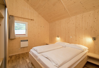 Schlafzimmer aus Holz mit Doppelbett, Nachttischen und Fenster in Kreischberg Chalets 21, Österreich.