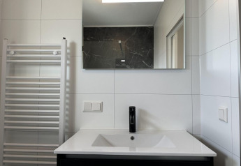 Moderno lavandino da bagno con rubinetto nero, specchio e scaldasalviette in Zonneweelde Lodge Deluxe, Paesi Bassi.