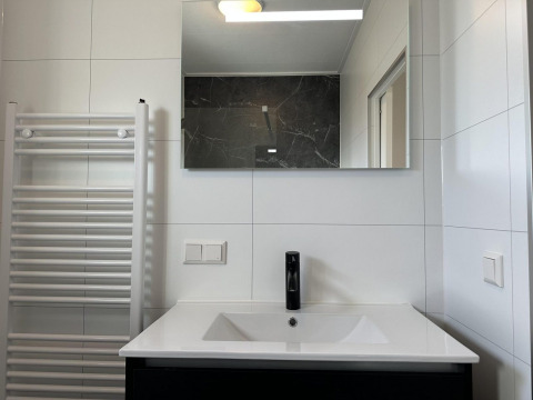Moderno lavabo de baño con grifo negro, espejo y radiador toallero en Zonneweelde Lodge Deluxe, Países Bajos.