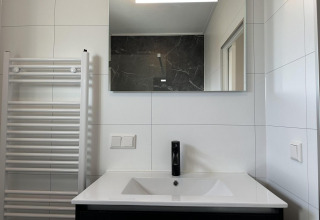 Moderno lavabo de baño con grifo negro, espejo y radiador toallero en Zonneweelde Lodge Deluxe, Países Bajos.