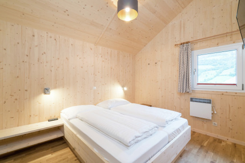 Helles Schlafzimmer mit Holzverkleidung, Doppelbett und Fenster im Kreischberg Chalets 21 in Österreich.