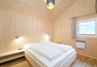 Helles Schlafzimmer mit Holzverkleidung, Doppelbett und Fenster im Kreischberg Chalets 21 in Österreich.