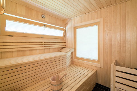Innenraum einer Holzsauna im Kreischberg Chalets 21, Österreich, mit Bank, Fenster und Wassereimer.