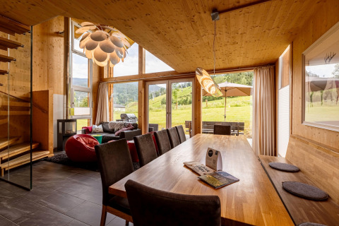 Modernes Wohnzimmer und Essbereich mit Holzdekor und Panoramafenstern in Kreischberg Chalets 21, Österreich.
