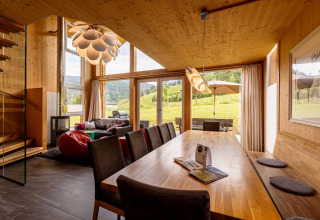 Modernes Wohnzimmer und Essbereich mit Holzdekor und Panoramafenstern in Kreischberg Chalets 21, Österreich.