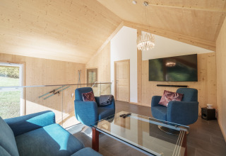 Lichte, moderne woonkamer in Kreischberg Chalets 27 in Oostenrijk met blauwe stoelen en grote tv.