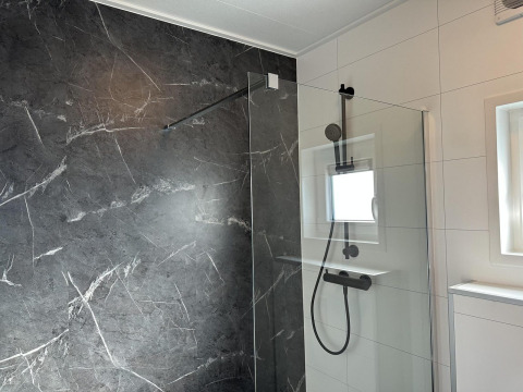 Moderne douche met donkere marmeren wand en glazen paneel in Zonneweelde Lodge Deluxe, Nederland.