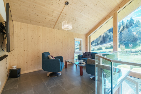 Moderne woonkamer in Kreischberg Chalets 27, Oostenrijk, met grote ramen, blauwe stoelen en natuuruitzicht.