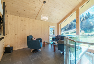 Moderne woonkamer in Kreischberg Chalets 27, Oostenrijk, met grote ramen, blauwe stoelen en natuuruitzicht.