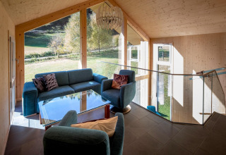 Zithoek met blauwe banken, glazen tafel en grote ramen bij Kreischberg Chalets 27, Oostenrijk.