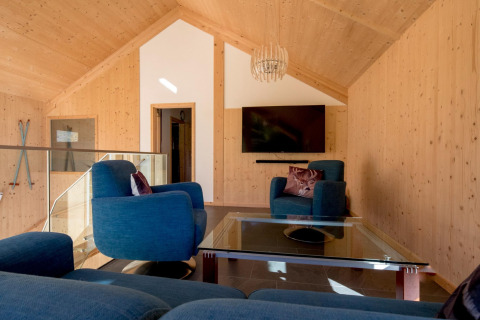 Woonkamer bij Kreischberg Chalets 27 in Oostenrijk met houten wanden, blauwe stoelen, glazen tafel en tv.