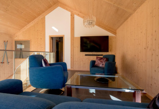 Woonkamer bij Kreischberg Chalets 27 in Oostenrijk met houten wanden, blauwe stoelen, glazen tafel en tv.
