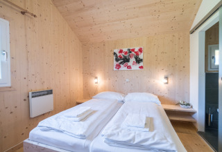 Lichte slaapkamer met twee eenpersoonsbedden, houten muren en kunstwerk in Kreischberg Chalets 27 in Oostenrijk.