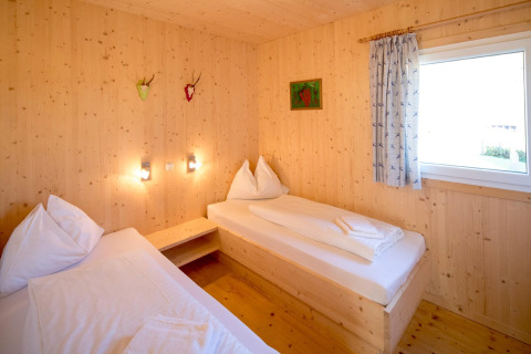 Kamer met twee eenpersoonsbedden, houten muren, raam en decoratie in Kreischberg Chalets 27, Oostenrijk.
