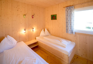 Kamer met twee eenpersoonsbedden, houten muren, raam en decoratie in Kreischberg Chalets 27, Oostenrijk.