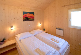 Lichte slaapkamer met twee eenpersoonsbedden, houten muren en raam in Kreischberg Chalets 27, Oostenrijk.