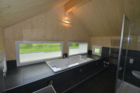Moderne badkamer met jacuzzi, grote ramen met uitzicht op groen, houten plafond en zwarte tegels.