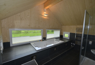 Moderne badkamer met jacuzzi, grote ramen met uitzicht op groen, houten plafond en zwarte tegels.