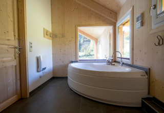 Lichte badkamer met hoekbad en grote ramen in Kreischberg Chalets 27, Oostenrijk, met uitzicht op het groen.