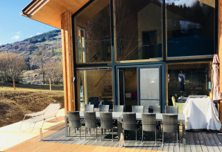Zonnig terras bij Kreischberg Chalets 27 in Oostenrijk met eettafel, ligstoel en uitzicht op de bergen.