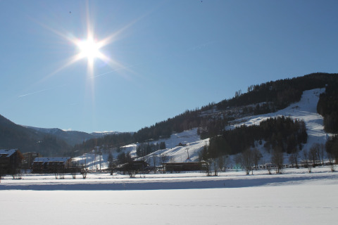 Sonniger Wintertag mit verschneiten Bergen und Hütten, gesehen von einer Berghütte aus.
