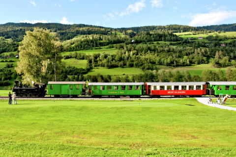 Historischer Dampfzug fährt an einer Glamping-Unterkunft vorbei, umgeben von grüner Landschaft und Hügeln.