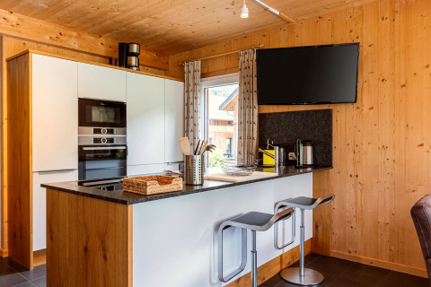 Moderne Küche aus Holz mit Frühstücksbar, Hockern, Flachbildfernseher und Fenster in Kreischberg Chalets 26, Österreich.