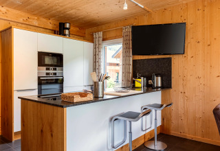 Moderne Küche aus Holz mit Frühstücksbar, Hockern, Flachbildfernseher und Fenster in Kreischberg Chalets 26, Österreich.