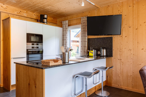 Moderne Küche aus Holz mit Frühstücksbar, Hockern, Flachbildfernseher und Fenster in Kreischberg Chalets 26, Österreich.