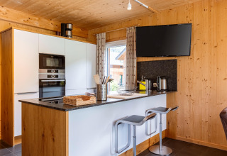 Moderne Küche aus Holz mit Frühstücksbar, Hockern, Flachbildfernseher und Fenster in Kreischberg Chalets 26, Österreich.
