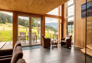 Wohnzimmer mit großen Fenstern, Holzdekor und Blick auf Wiesen und Berge in den Kreischberg Chalets 26, Österreich.