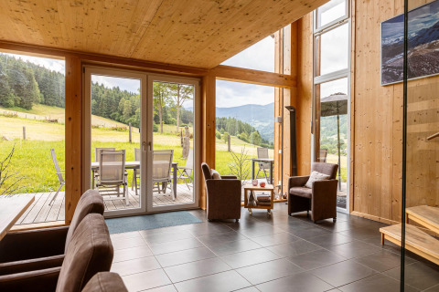 Wohnzimmer mit großen Fenstern, Holzdekor und Blick auf Wiesen und Berge in den Kreischberg Chalets 26, Österreich.