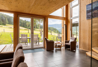 Wohnzimmer mit großen Fenstern, Holzdekor und Blick auf Wiesen und Berge in den Kreischberg Chalets 26, Österreich.