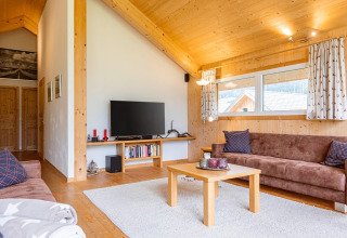 Wohnzimmer im Kreischberg Chalets 26 in Österreich mit braunen Sofas, Holzdecke und Fernseher.