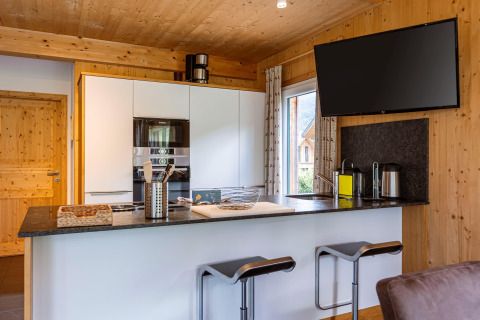 Moderne Küche mit Holzdekor in Kreischberg Chalets 26, Österreich, Barhocker und großem Flachbild-TV.
