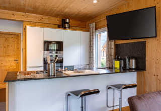 Moderne Küche mit Holzdekor in Kreischberg Chalets 26, Österreich, Barhocker und großem Flachbild-TV.
