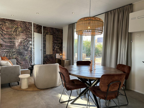 Salón comedor moderno con mesa redonda, sillas marrones y pared de hojas en Zonneweelde Lodge Deluxe.