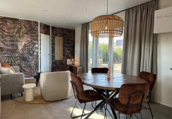 Salon et salle à manger modernes avec table ronde, chaises marron et mur feuillu à Zonneweelde Lodge Deluxe.