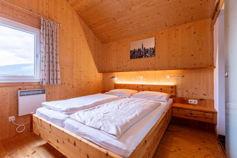 Schlafzimmer mit Holzbett, großem Fenster und moderner Dekoration im Kreischberg Chalets 26 in Österreich.