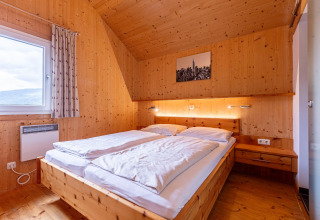 Schlafzimmer mit Holzbett, großem Fenster und moderner Dekoration im Kreischberg Chalets 26 in Österreich.