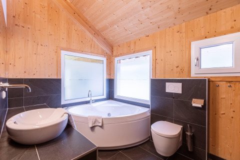 Modernes Badezimmer mit Holzverkleidung, Eckbadewanne und großen Fenstern in den Kreischberg Chalets 26, Österreich.