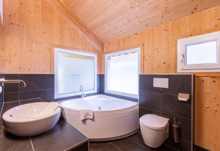 Modernes Badezimmer mit Holzverkleidung, Eckbadewanne und großen Fenstern in den Kreischberg Chalets 26, Österreich.