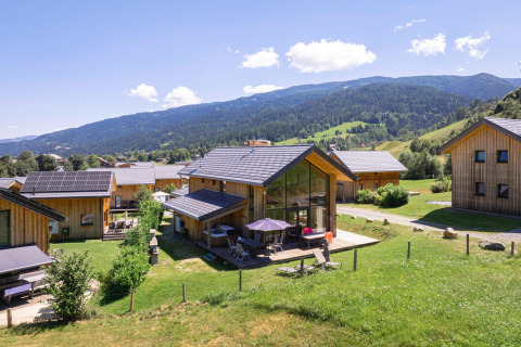 Moderne Holzhütten der Kreischberg Chalets 26 in Österreich mit Bergen im Hintergrund an einem sonnigen Tag.