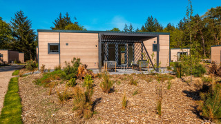 Moderne glamping accommodatie met houten bekleding, terrasstoelen en omgeven door natuur en bos.