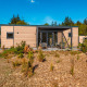 Modernes Glamping-Unterkunft aus Holz mit Terrasse inmitten natürlicher Landschaft und blauem Himmel.
