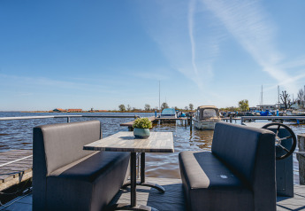 Zicht vanop Houseboat «Havenlodge Plus» in Marina Uitgeest, Nederland, met banken en aangemeerde boten.