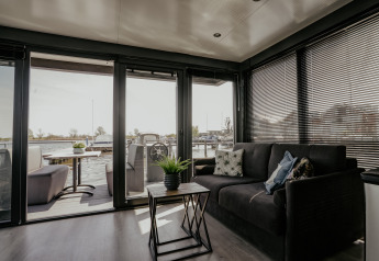 Zona giorno moderna nella houseboat Havenlodge Plus a Marina Uitgeest, con vista sulla terrazza e sull’acqua.