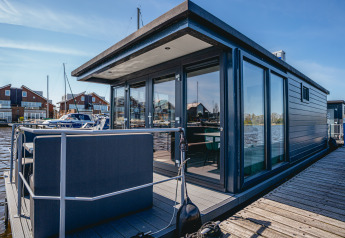 Modernes Hausboot Havenlodge Plus mit großer Fensterfront und Terrasse, vertäut am Steg bei Sonnenschein.