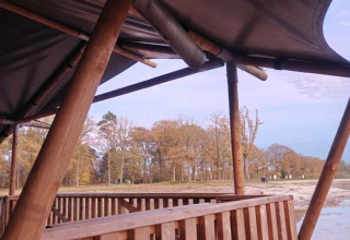 Zicht vanuit een safaritent met houten terras aan het meer op Camping De Rammelbeek in Nederland.