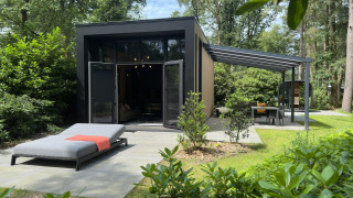 Moderne Veluwe Suite lodge met sauna, zonneterras en ligbed, omringd door het groene boslandschap.